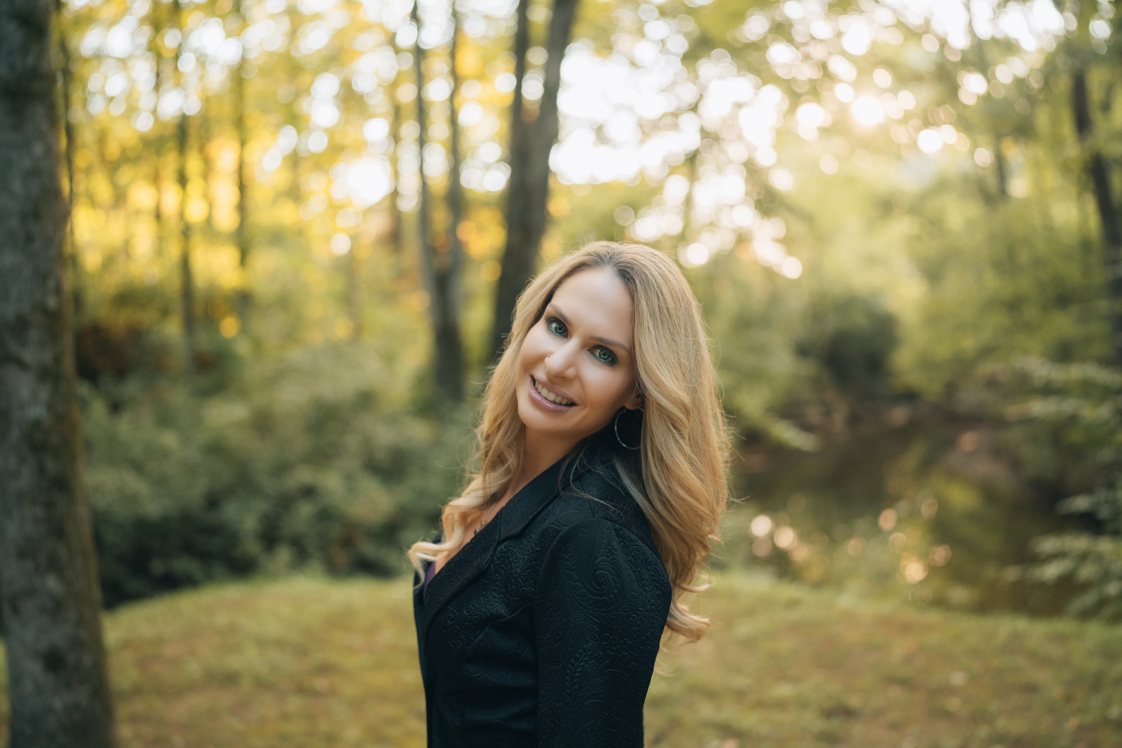 Roxanne Miller, LCSW, smiling in a sunlit forest clearing in autumn